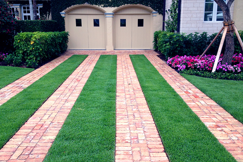 A cobble stone driveway with vibrant turfgrass inlays leading into a home garage 